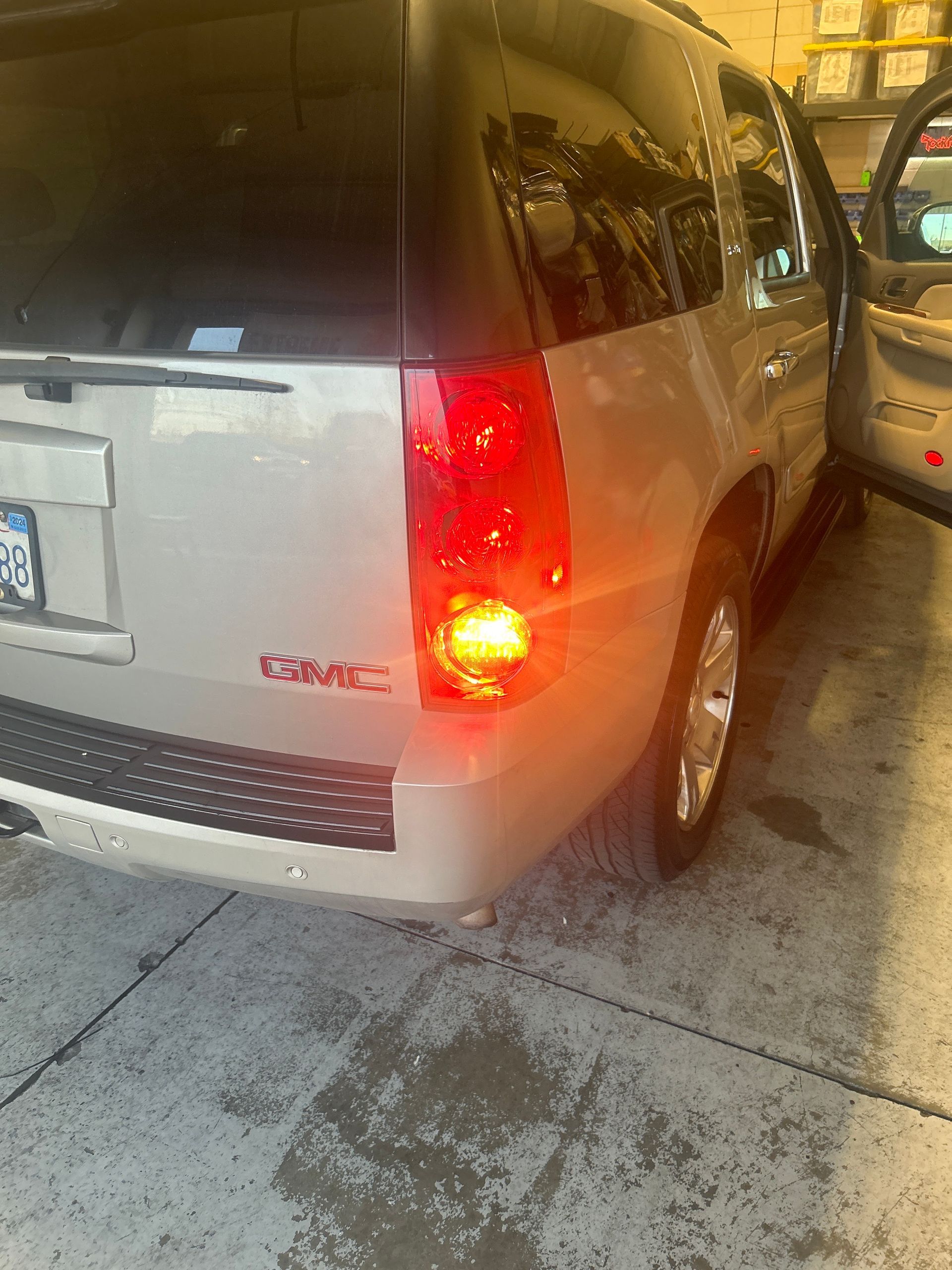 Silver van rear bumper in a parking garage, with red brake lights on and a car beside it.