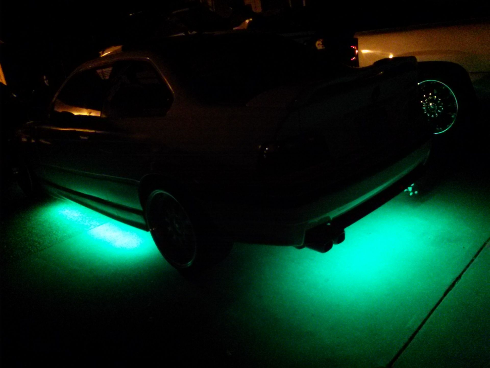 Dark car parked at night with bright green underglow lighting beneath it.