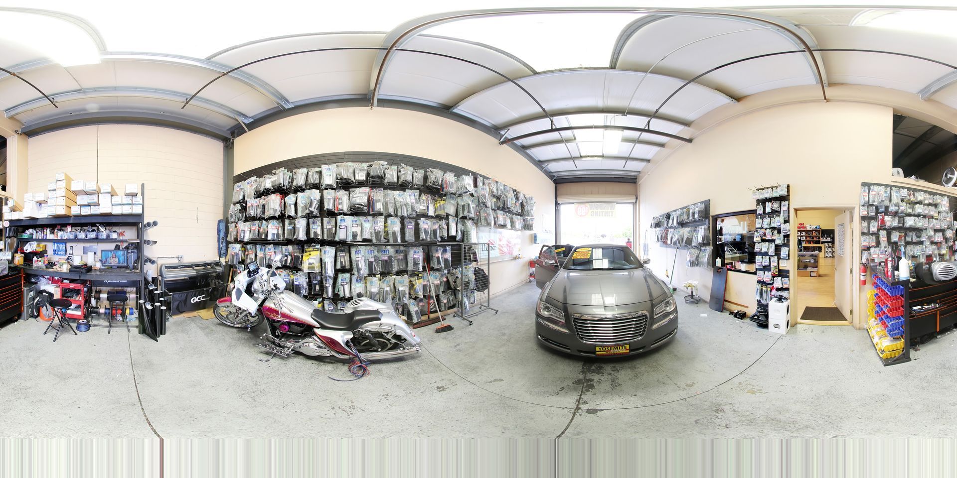 Wide auto garage with car lifts, several vehicles, and shelves of parts under a curved metal roof.