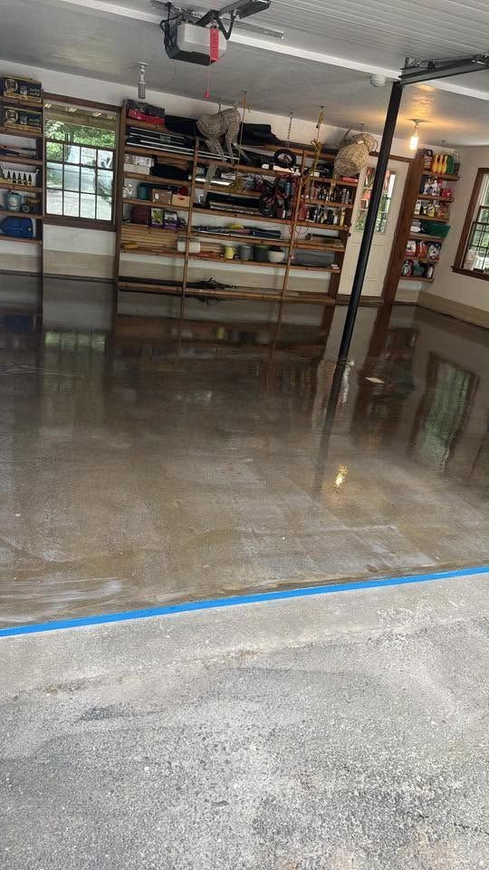 Person smoothing wet, gray flooring with a tool, wearing gloves and work clothes.