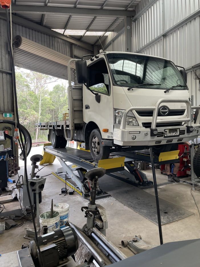 A White Hino Flatbed Truck Raised on a Hydraulic Lift — Berkeley Vale Tyre & Mechanical in Fountaindale, NSW