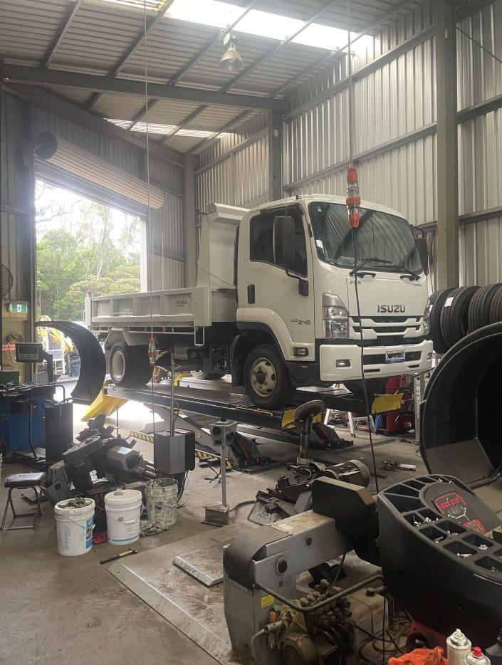 A White Isuzu Dump Truck Raised on a Hydraulic Lift — Berkeley Vale Tyre & Mechanical in Fountaindale, NSW