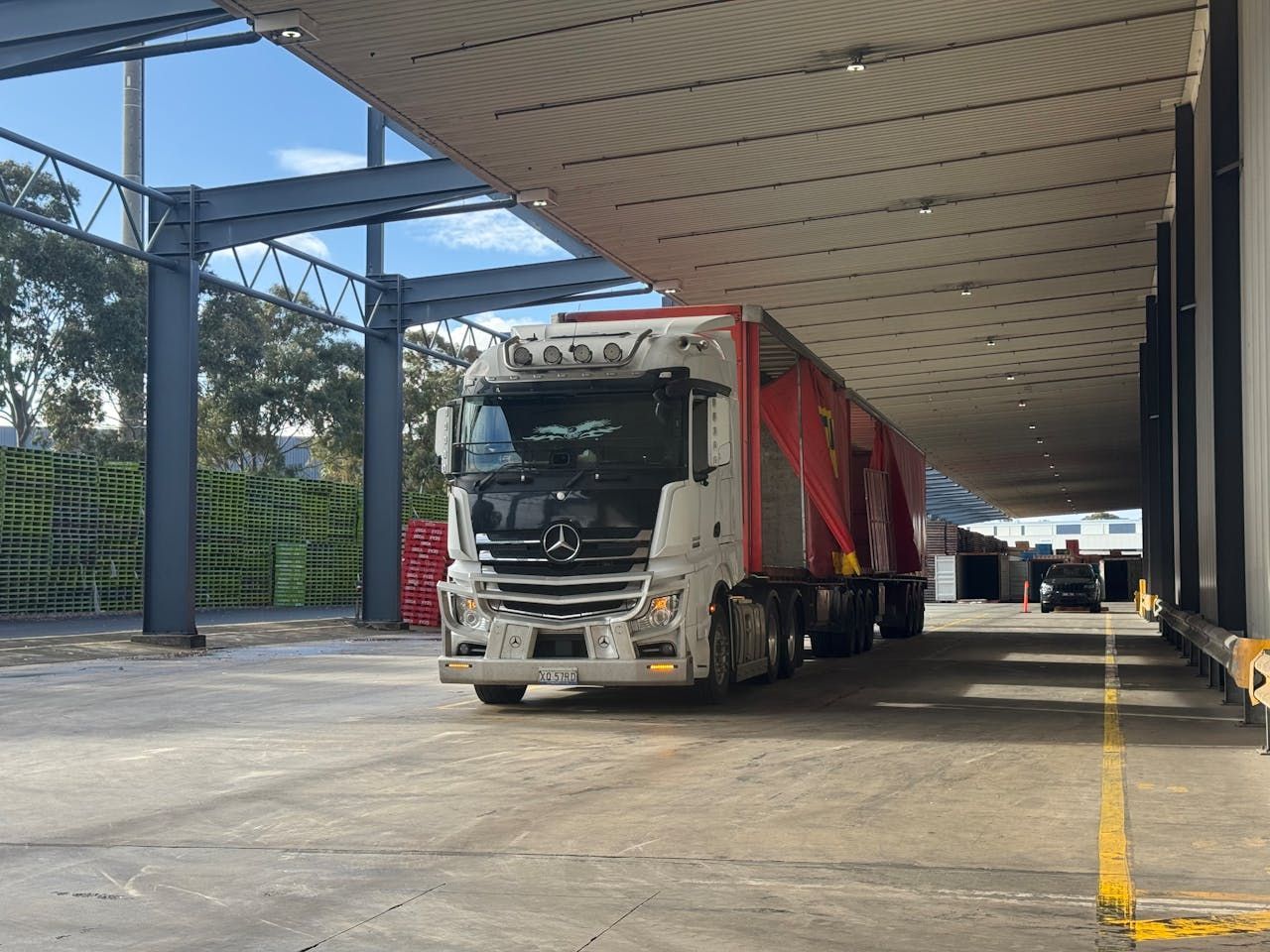 Cargo truck parked under a covered loading dock with a red trailer and white cab