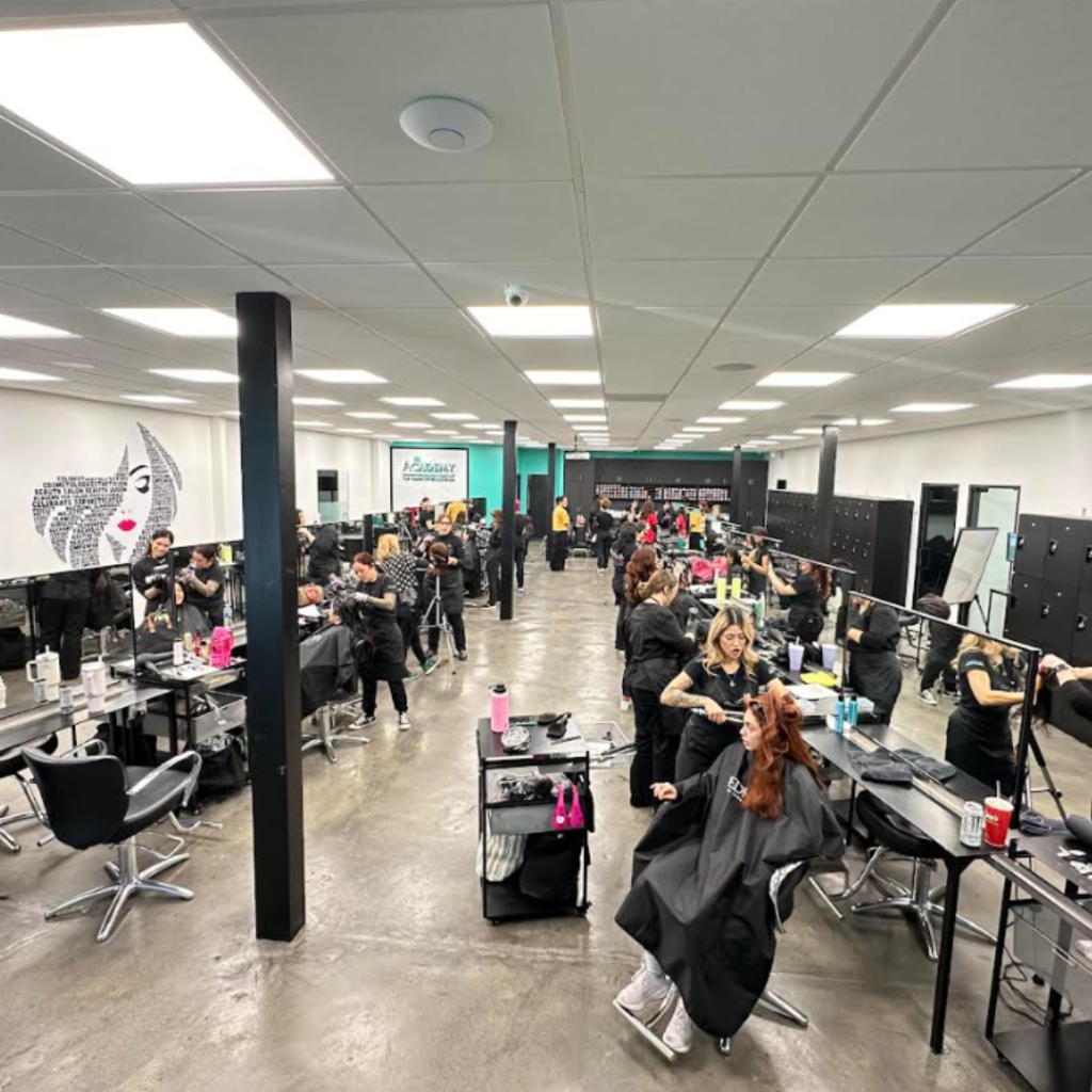 Busy salon training floor with many stylists working on clients at stations in a bright, open room