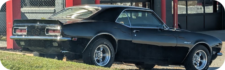 Black classic muscle car parked in front of a building, side view outdoors | West Main Auto Repair