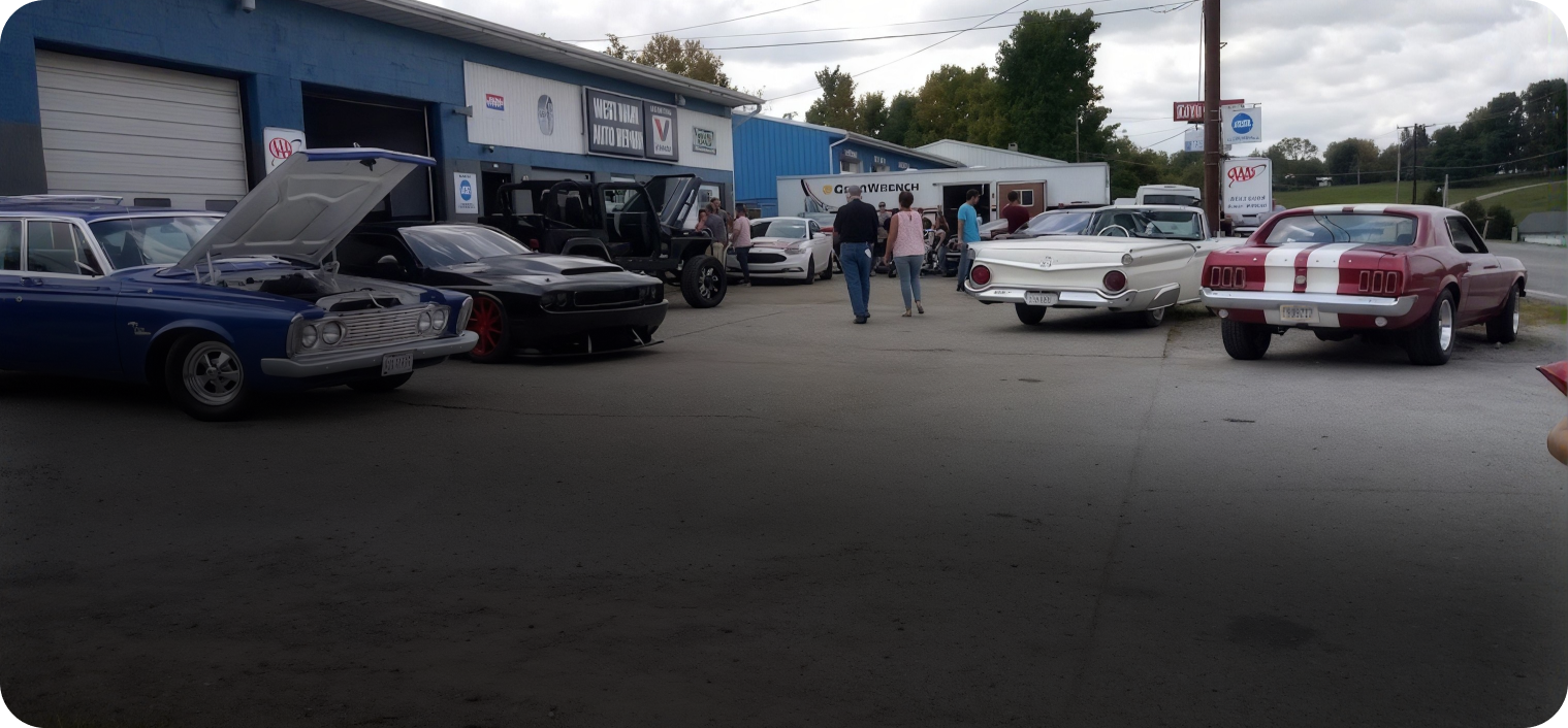 Classic cars parked outside a building, with people gathered in a lot on an overcast day. | West Main Auto Repair