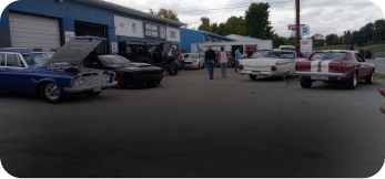 Classic cars parked outside a garage with people gathered in the lot | West Main Auto Repair