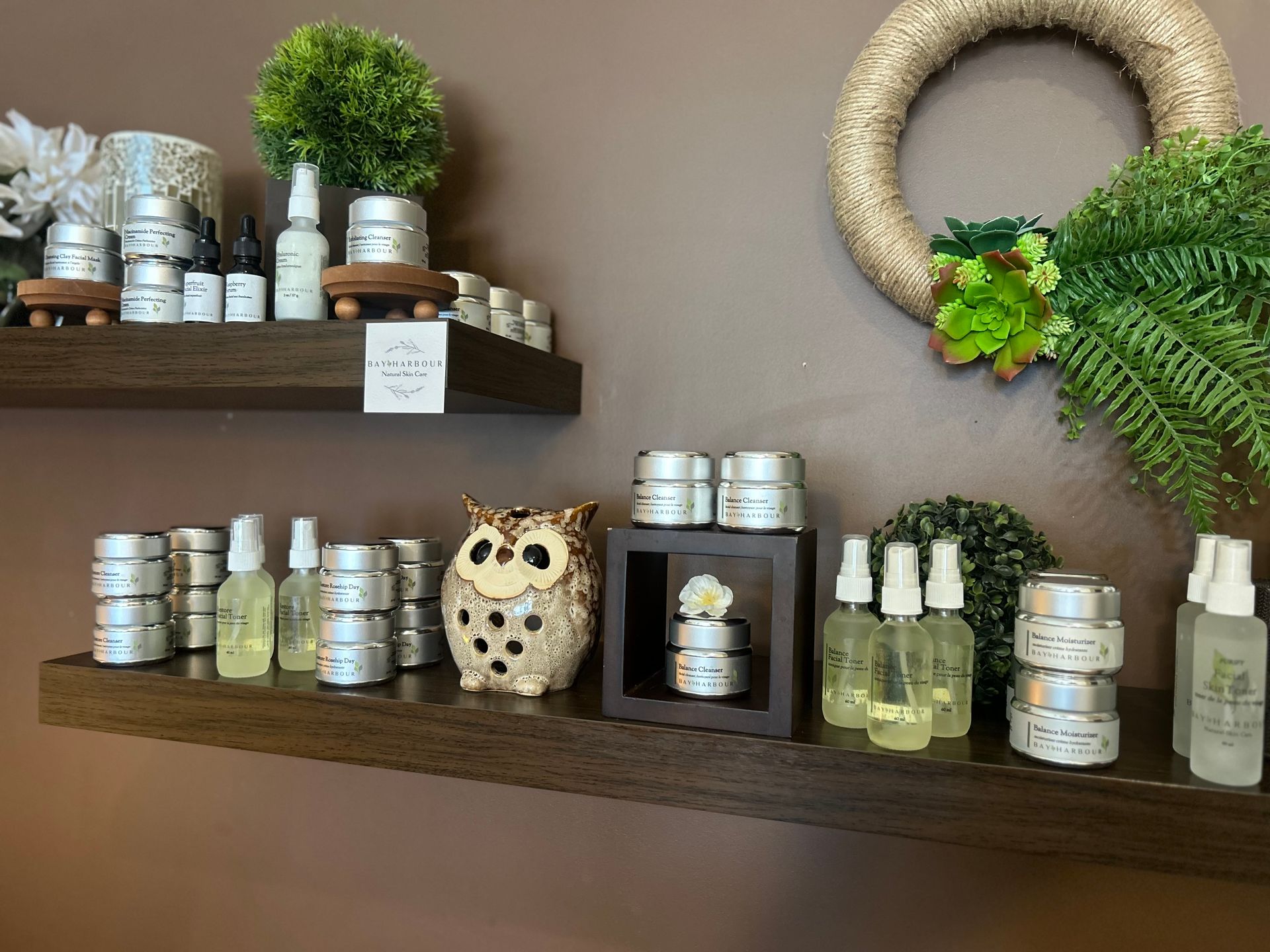 Shelves displaying various cosmetic products in silver tins and bottles, with decorative owl and greenery.