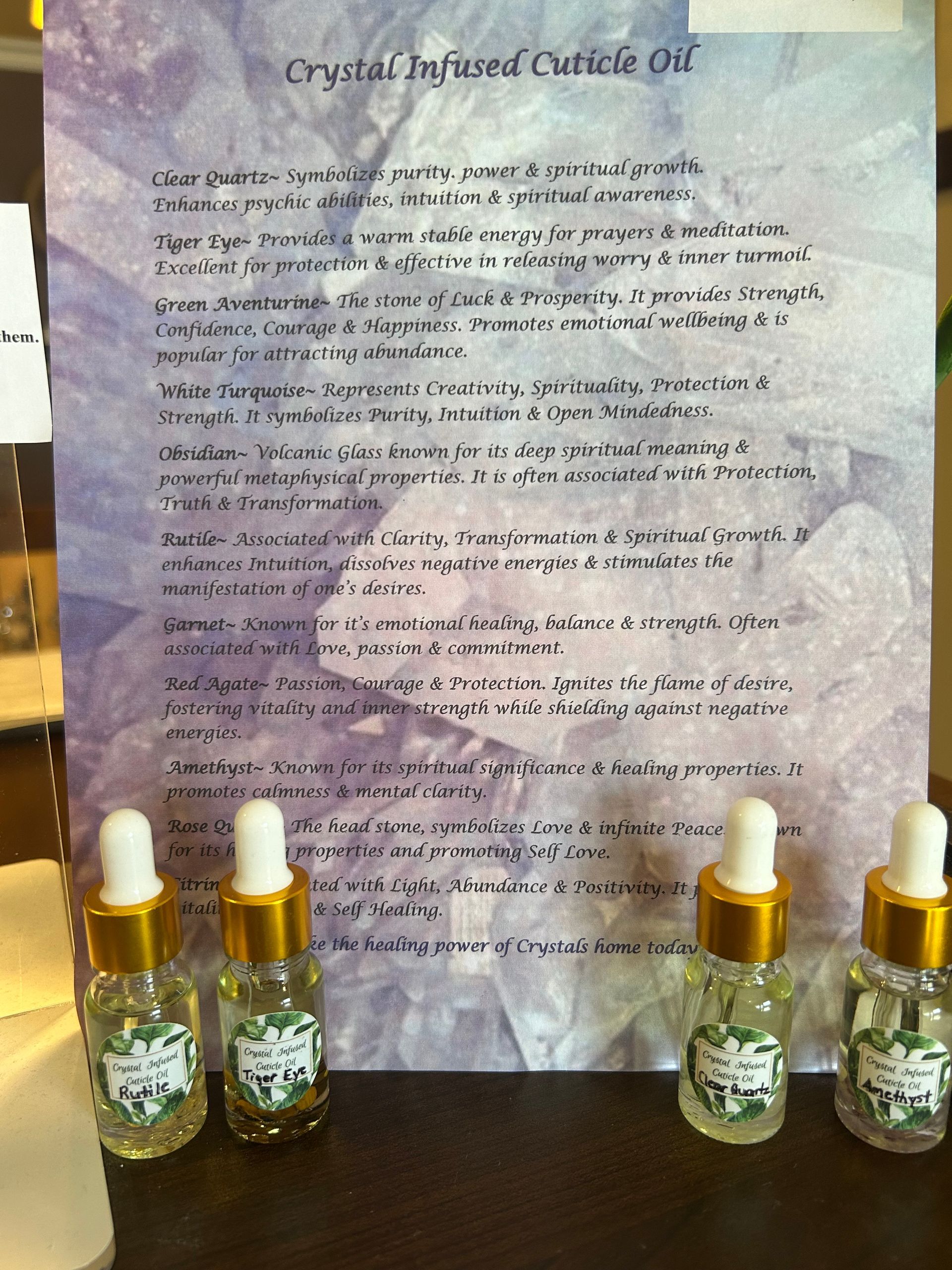 Four small bottles of crystal-infused cuticle oil with a printed description on a purple background.
