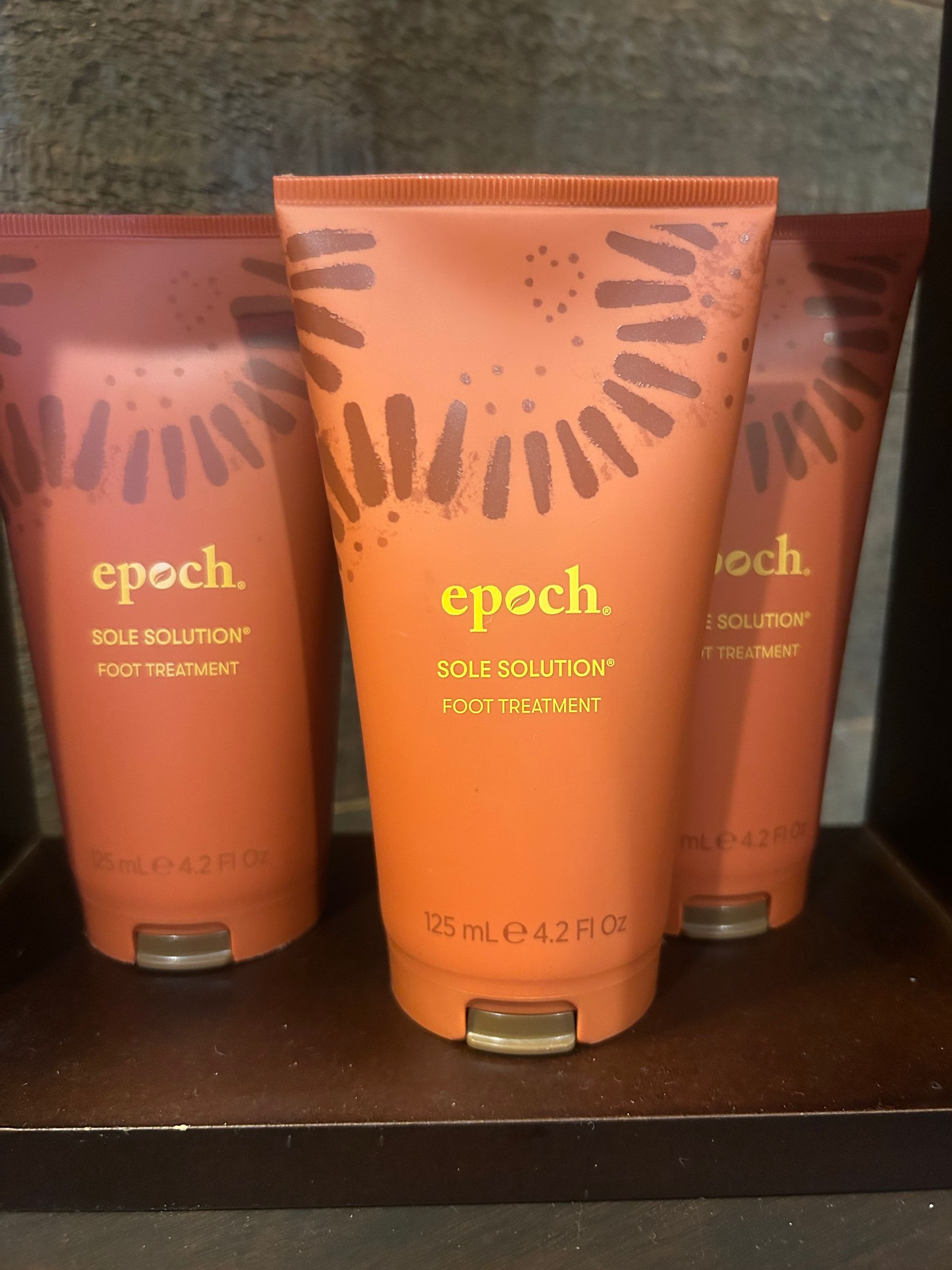 Three orange tubes of Epoch body moisturizer on a shelf, each with gold text and a sunburst design.