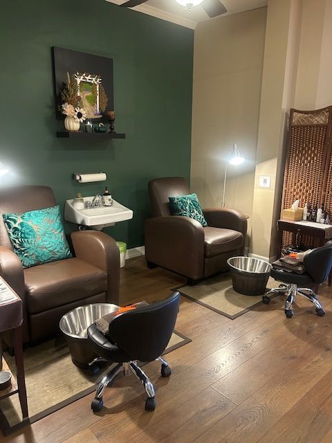 A pedicure room with two brown leather chairs, foot basins, and a dark green wall.