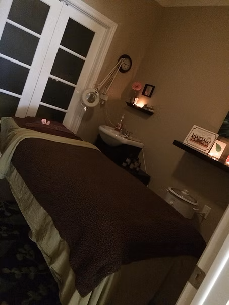 Spa treatment room with massage table, sink, and decorative shelves.