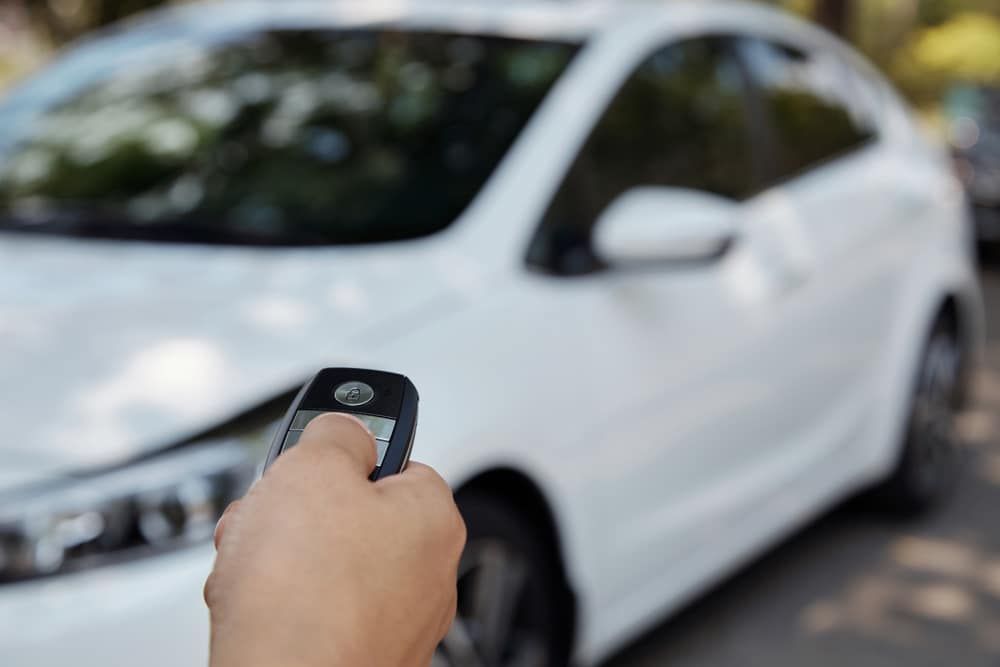 A Person is Holding a Remote Control in Front of a White Car — Coffs City Lockmart Pty Ltd in North Boambee Valley, NSW