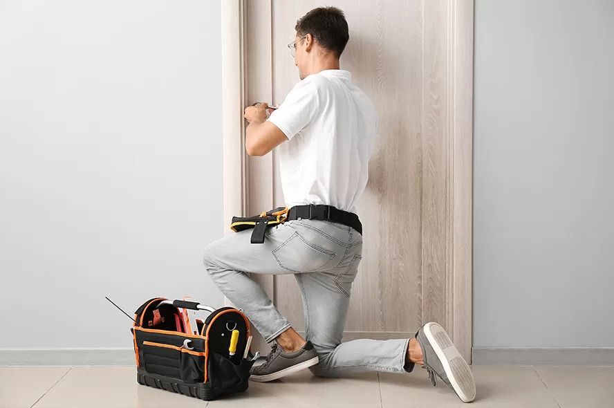 A Man Is Kneeling Down in Front of A Door While Fixing It — Coffs City Lockmart Pty Ltd in North Boambee Valley, NSW