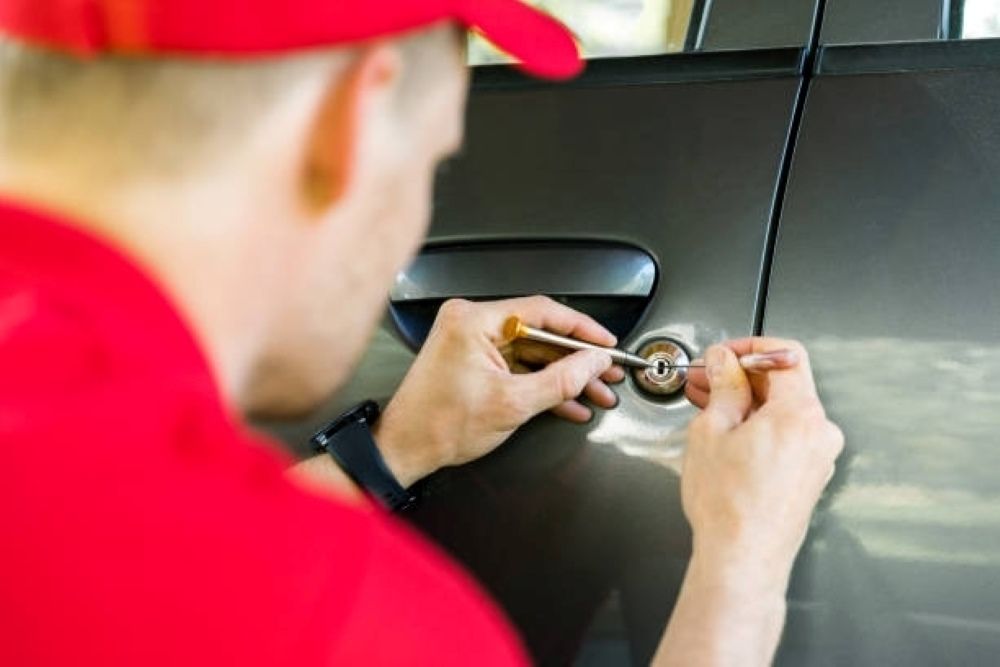 A Man in a Red Hat is Opening a Car Door With a Screwdriver — Coffs City Lockmart Pty Ltd in Nambucca Heads, NSW
