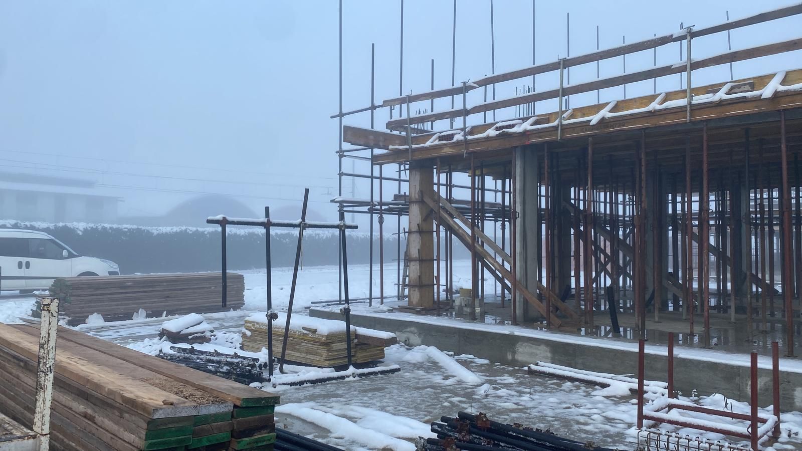 Cantiere edile innevato con impalcature e una struttura parzialmente costruita in una giornata nebbiosa.