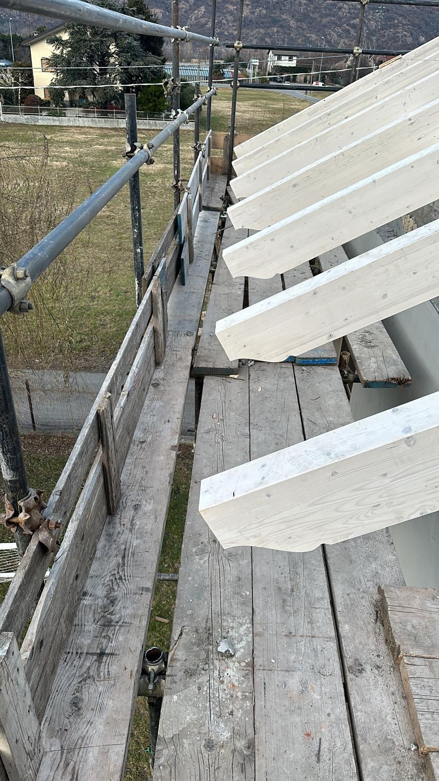 Scalinate di legno consumate dal tempo con panchine bianche accanto a un campo recintato sotto un cielo nuvoloso.