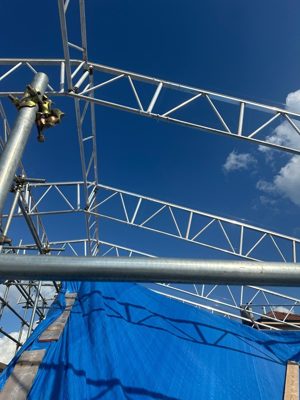 Struttura metallica del palcoscenico contro un cielo azzurro, con un telone blu in primo piano.