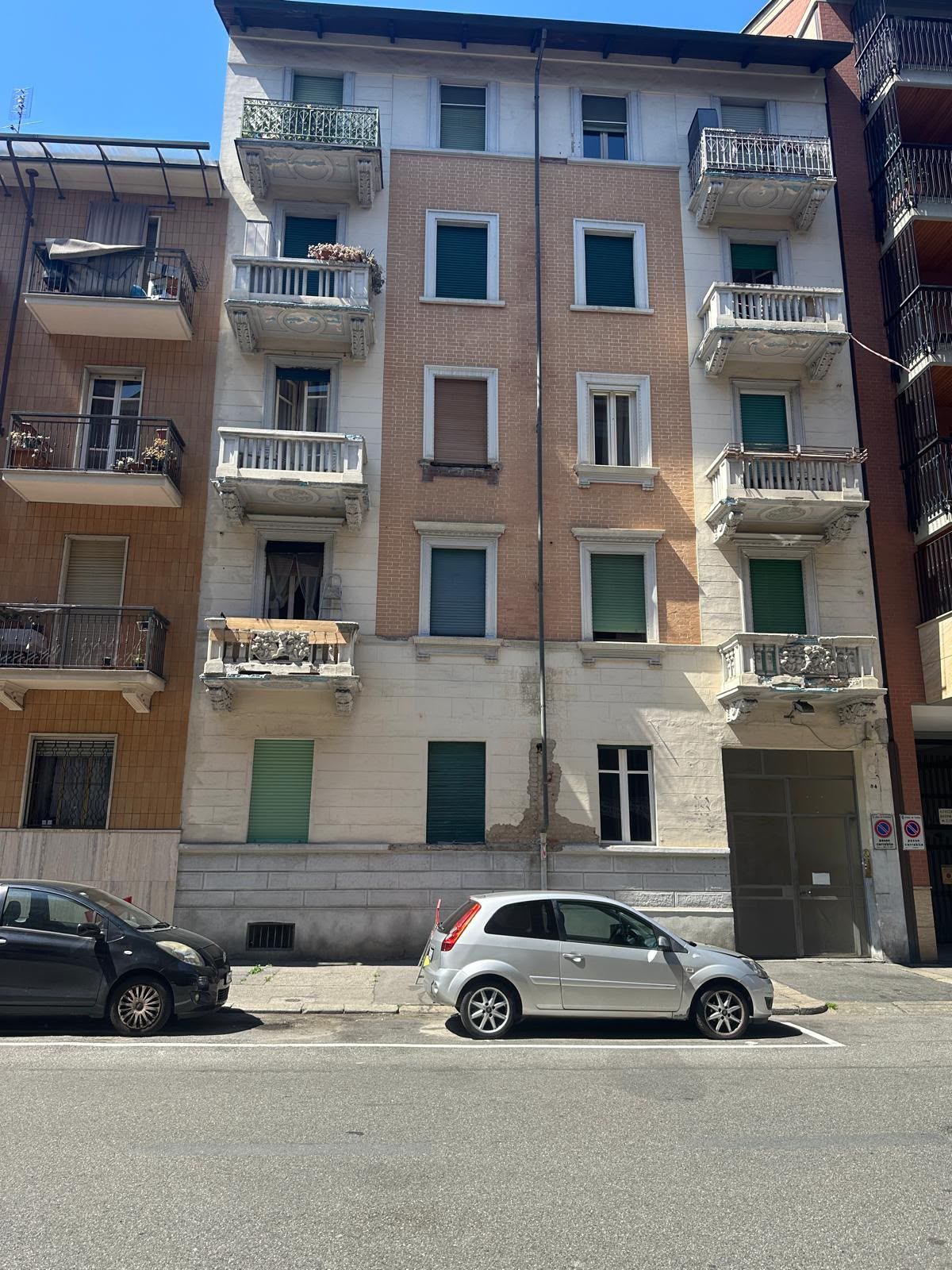 Palazzo residenziale con balconi e auto parcheggiate su una strada soleggiata