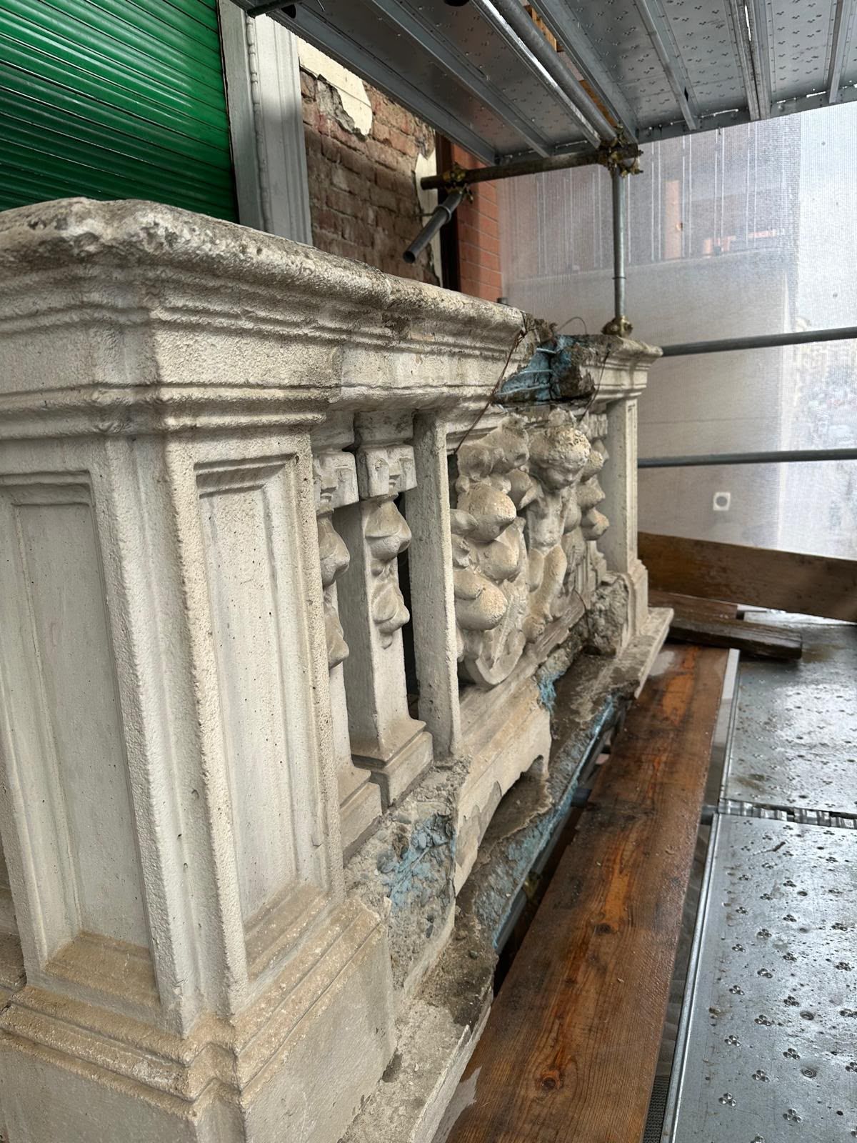 Frammento di altare o tomba in pietra bianca e polverosa, finemente decorata, appoggiato in un locale adibito a deposito o restauro.