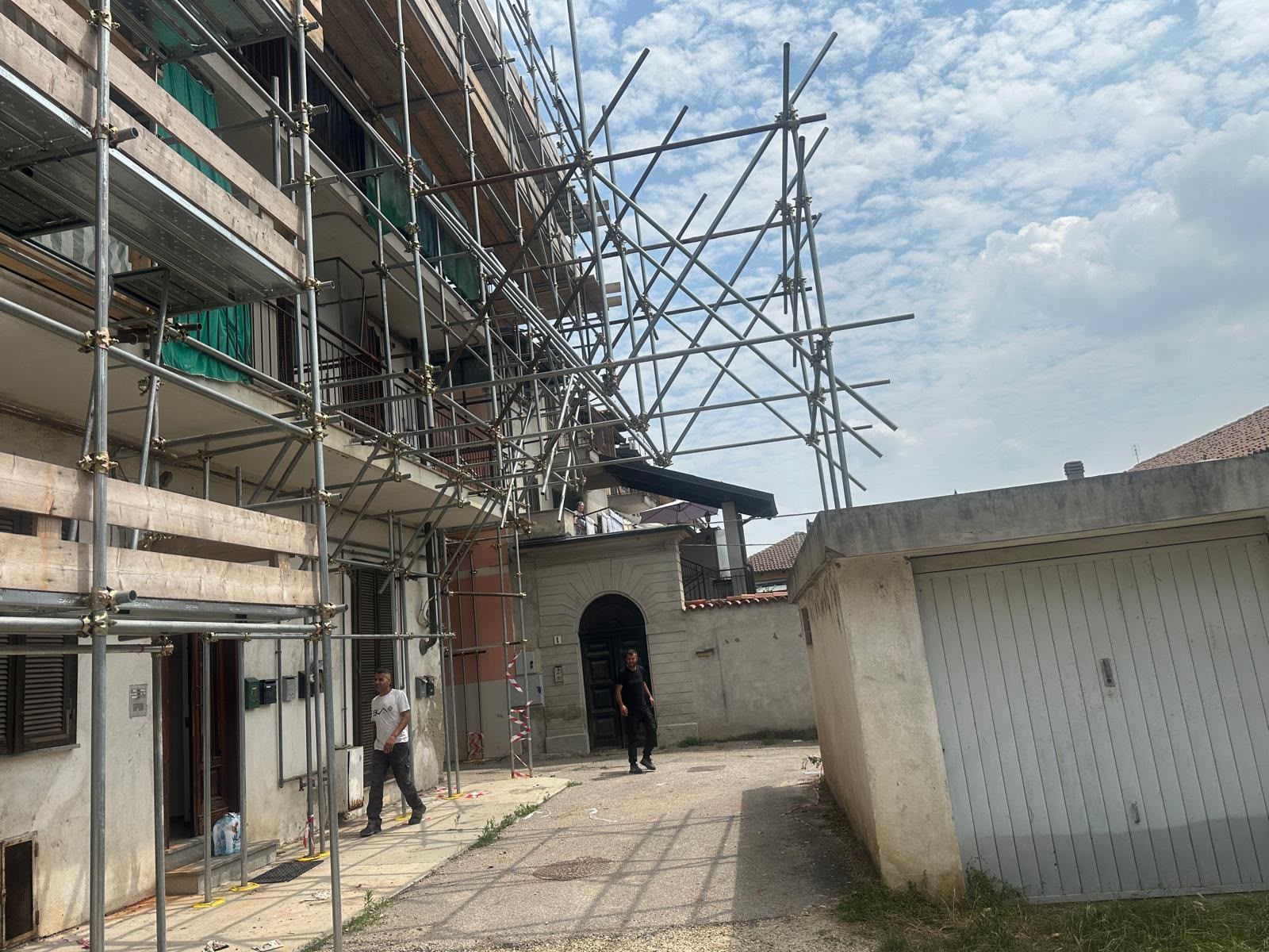 Impalcature accanto a un edificio in ristrutturazione, con una persona che cammina in un cortile lastricato.