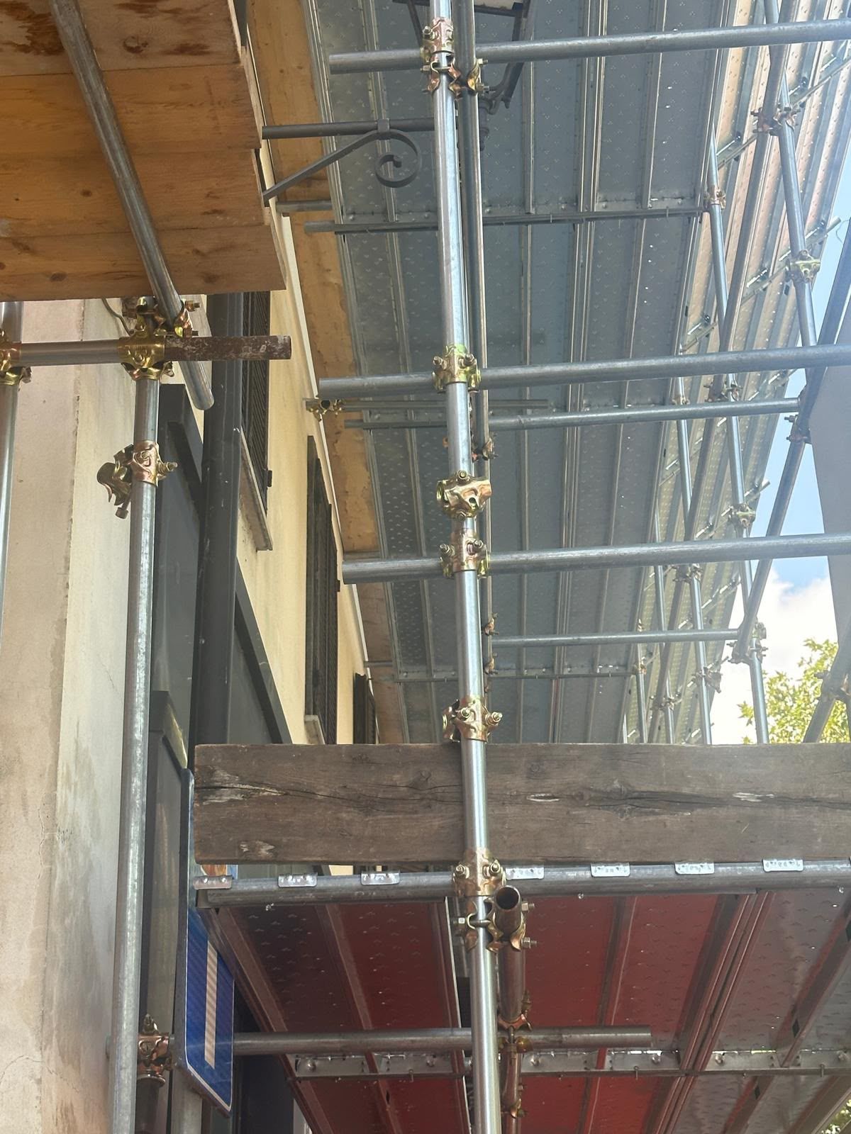 Impalcature e assi di legno accanto a un edificio in costruzione, con un telone rosso sottostante.