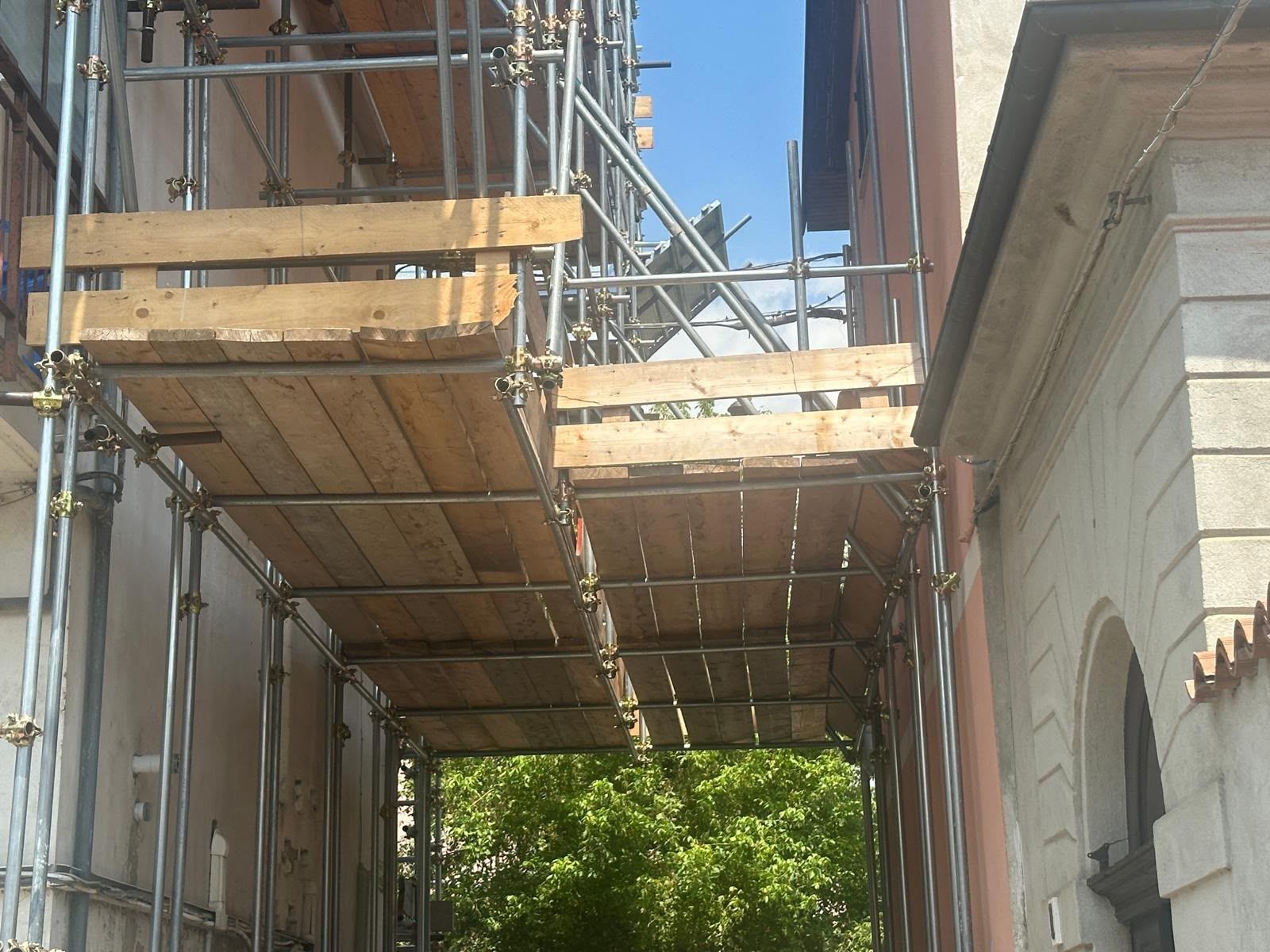 Passerella impalcata tra gli edifici, con assi di legno e supporti metallici, attualmente in costruzione.