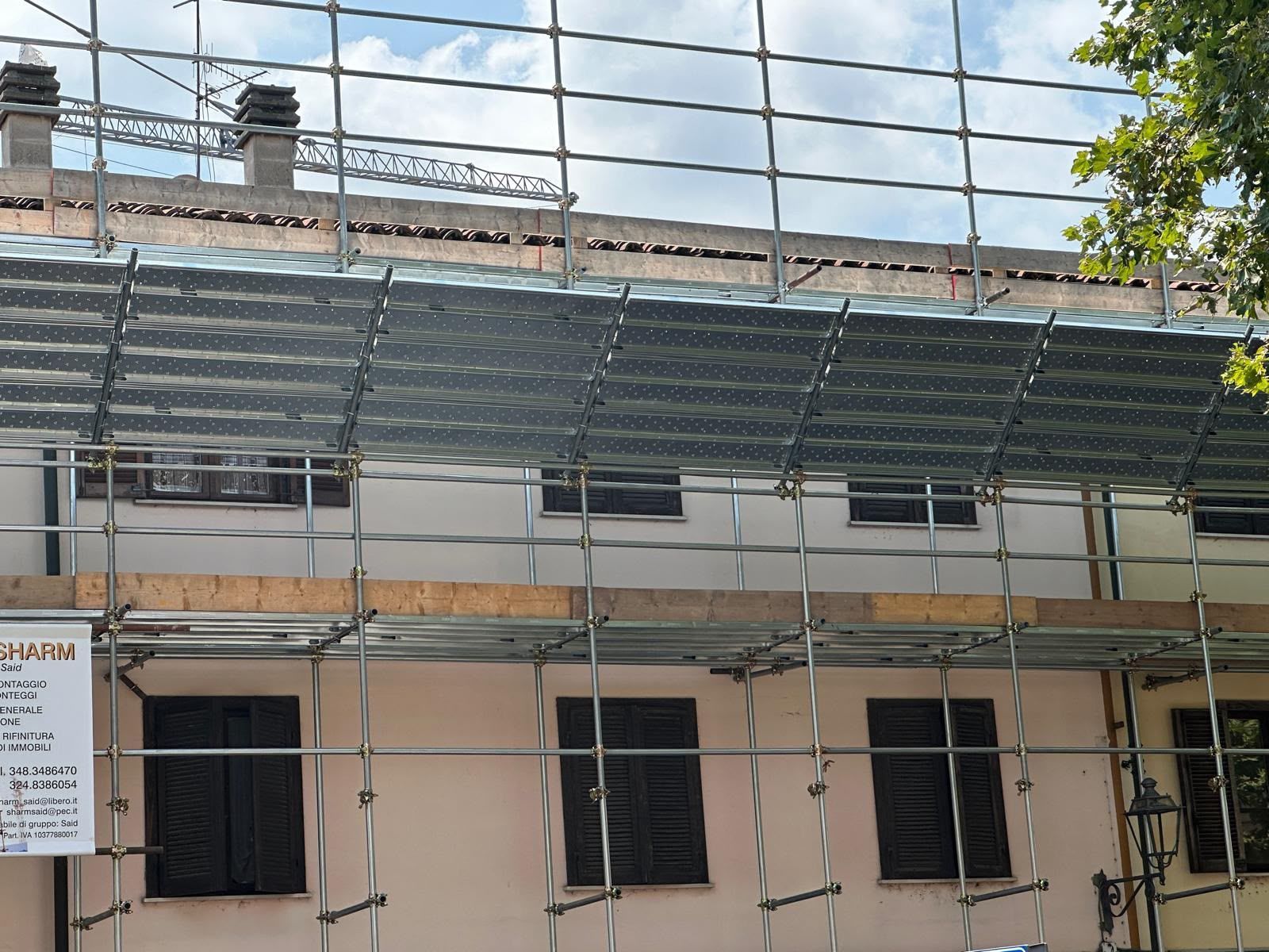 Edificio in costruzione con impalcature verdi e rete metallica su pareti beige.