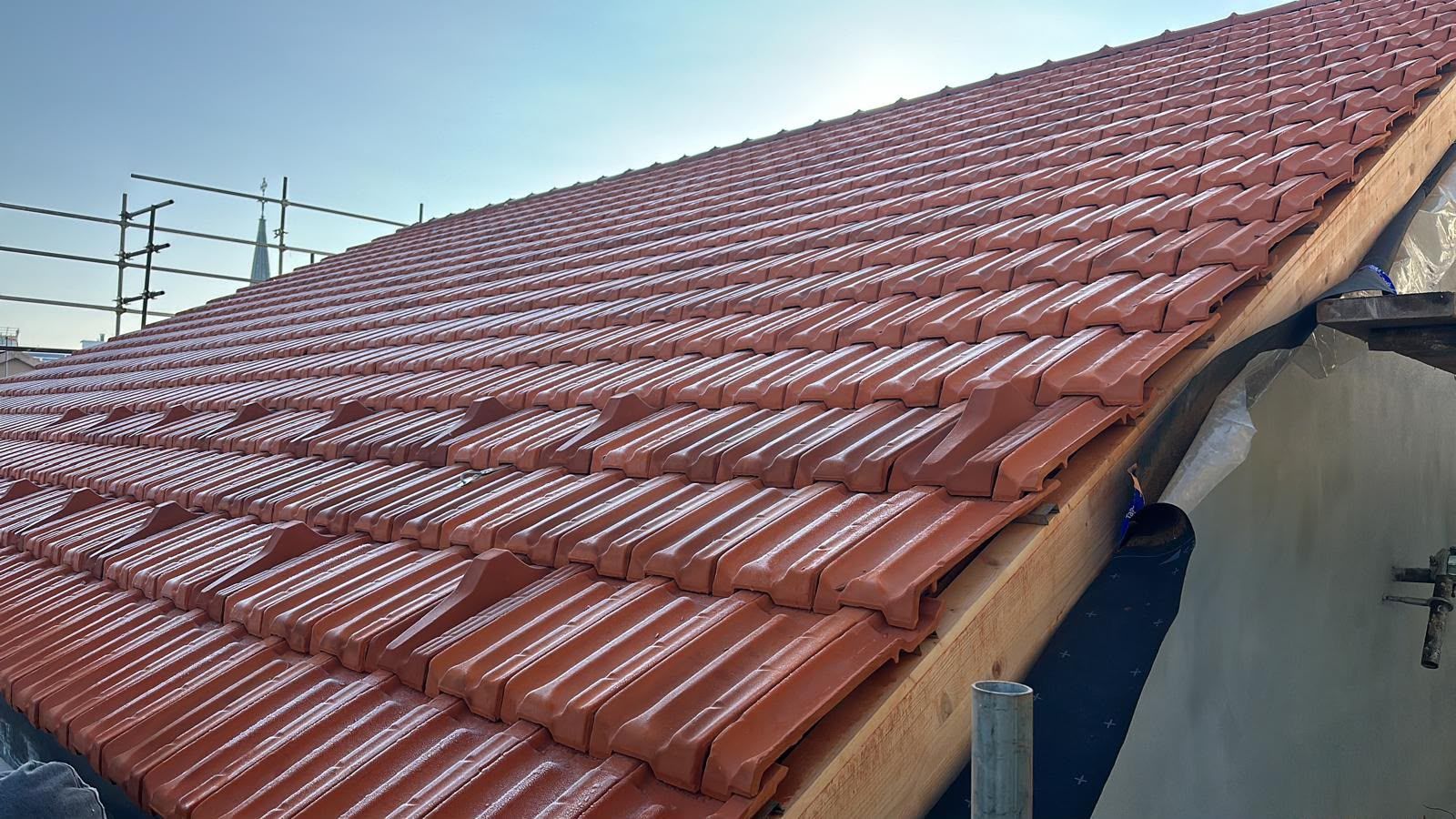Tetto di tegole rosse su un edificio, visto di profilo sotto un cielo limpido.