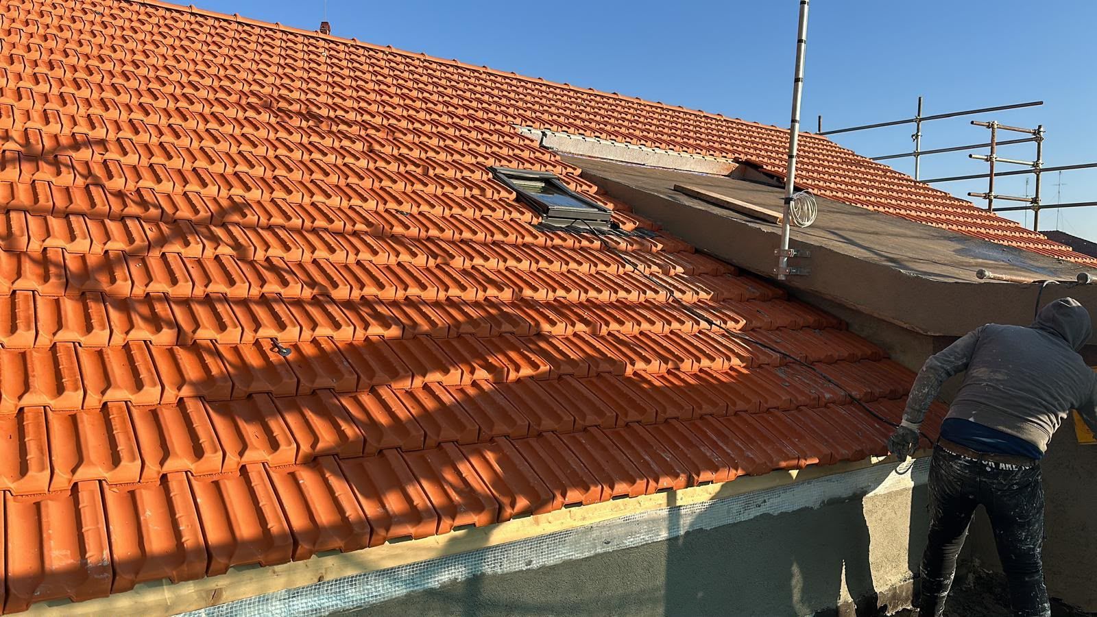 Un operaio installa pannelli solari su un tetto di tegole rosse sotto un cielo sereno.