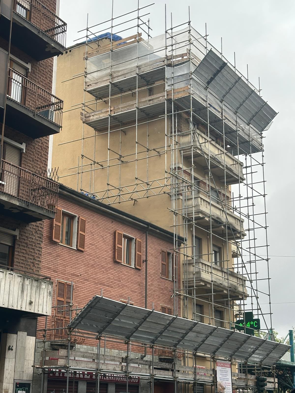 Facciata di un edificio in costruzione, impalcata, accanto a un edificio in mattoni su una strada cittadina.
