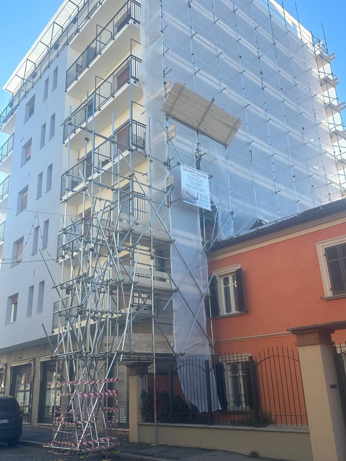 Impalcature avvolgono un palazzo bianco accanto a una casa rossa sotto un cielo azzurro.