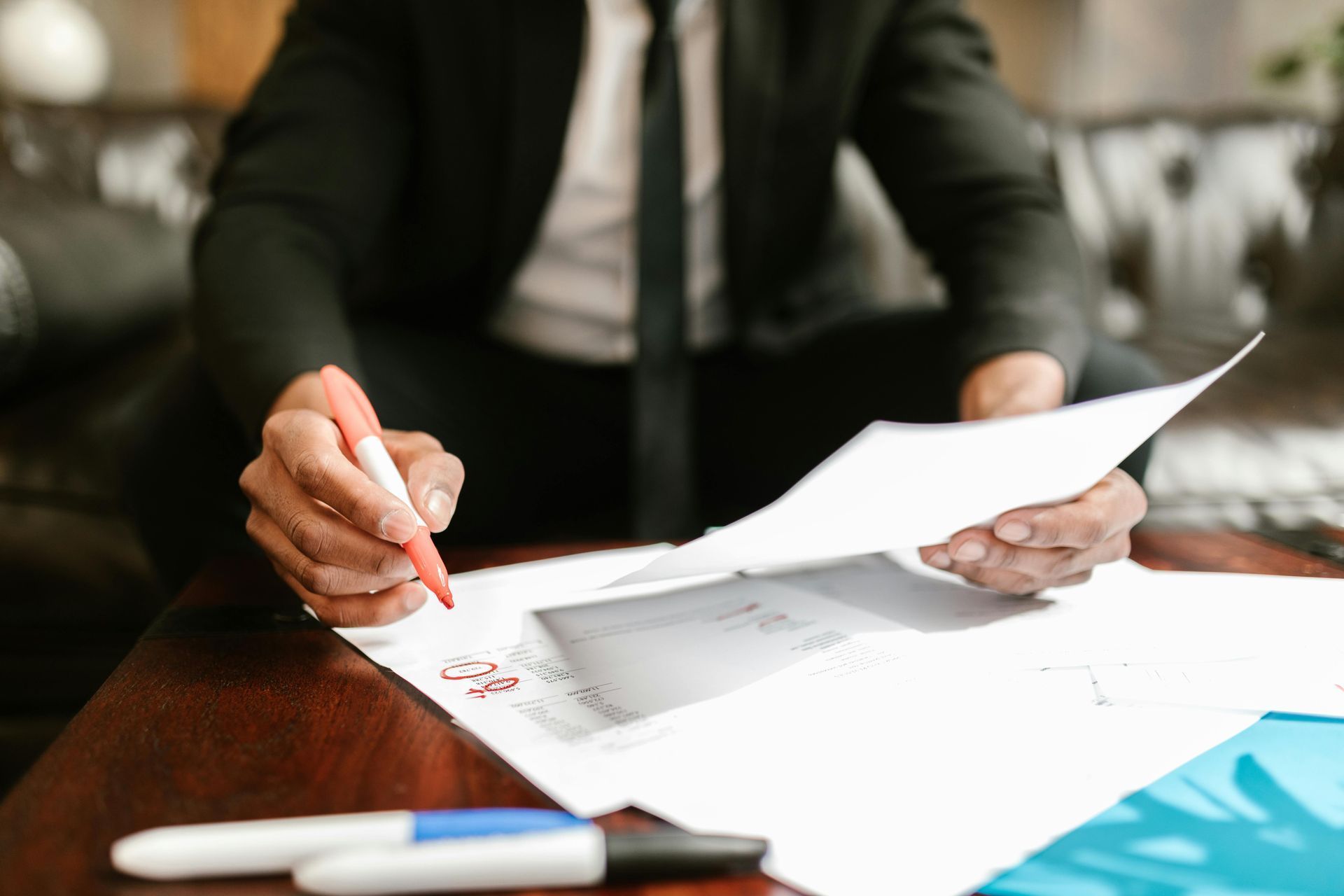 A person in a business suit reviews and marks document papers at a table with markers.