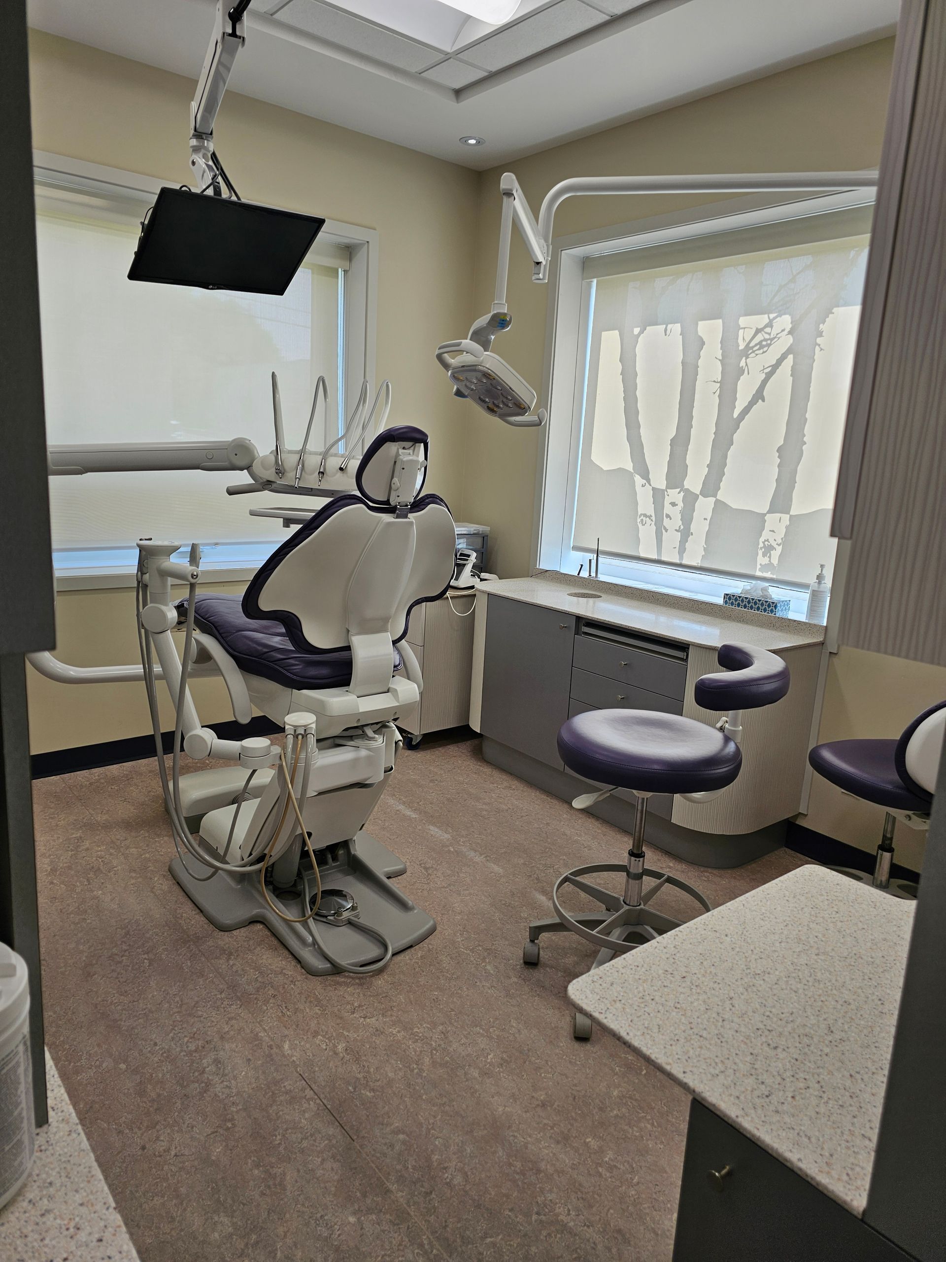 A dental examination room with a chair, medical equipment, and stools under a bright skylight.