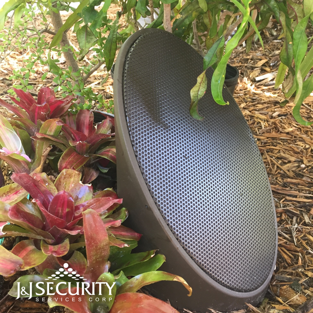 Brown outdoor speaker hidden among plants and mulch.