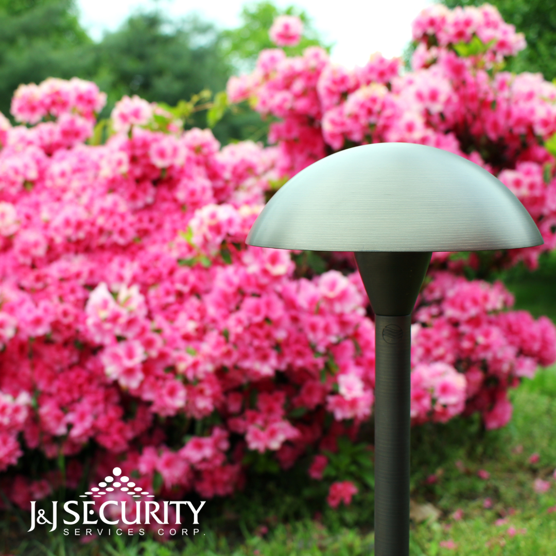 Bronze landscape light in front of pink blooming azalea bush.