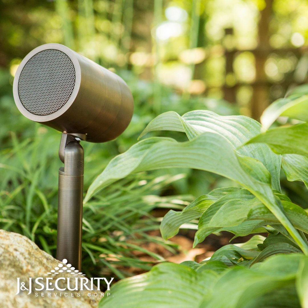 Bronze outdoor speaker in a garden setting, positioned near plants.
