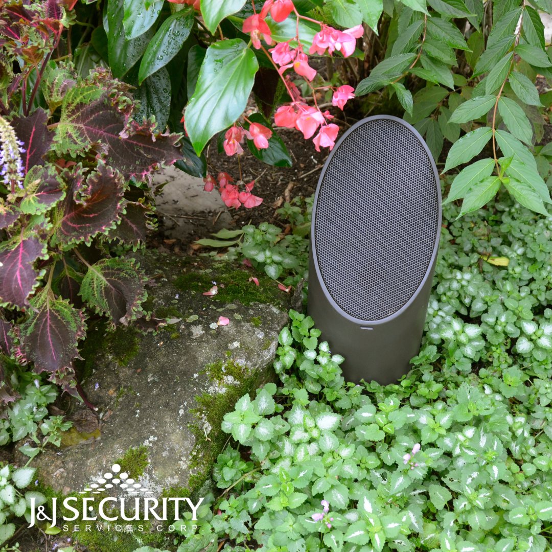 Brown outdoor speaker in a garden with plants and flowers.