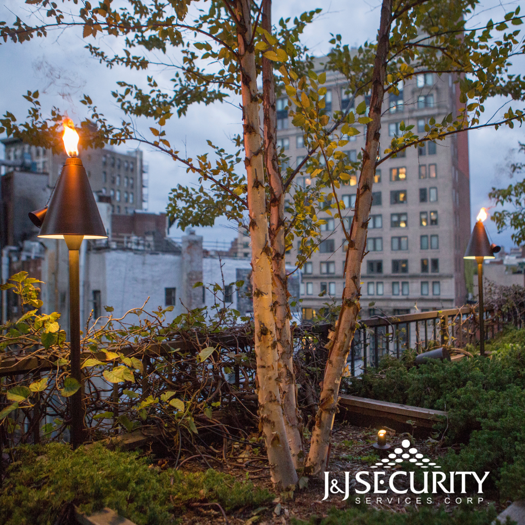 Rooftop with tiki torches, trees, and city buildings in the background at dusk.
