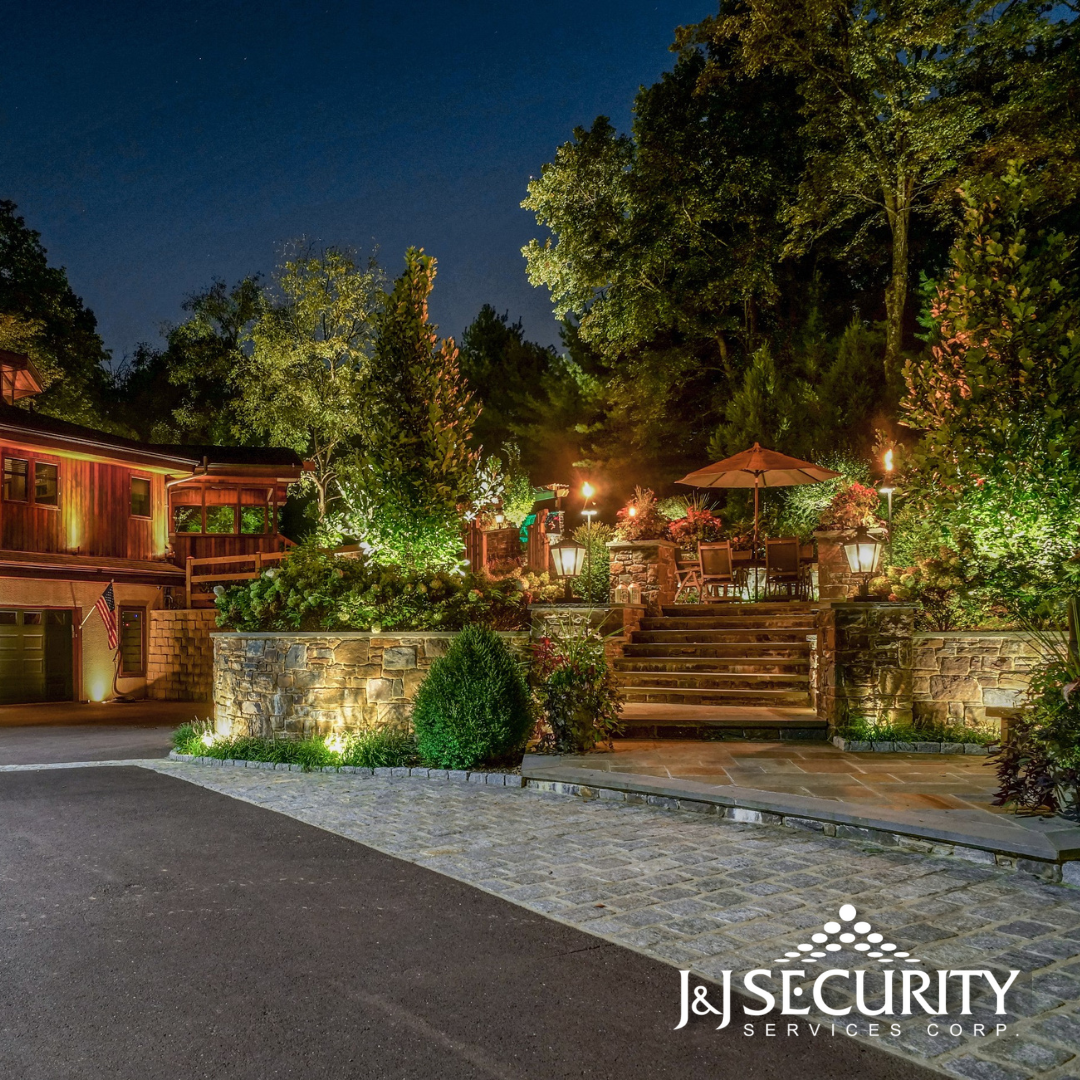 Nighttime view of a house with illuminated landscaping and outdoor dining area. Stone steps lead up to a patio.