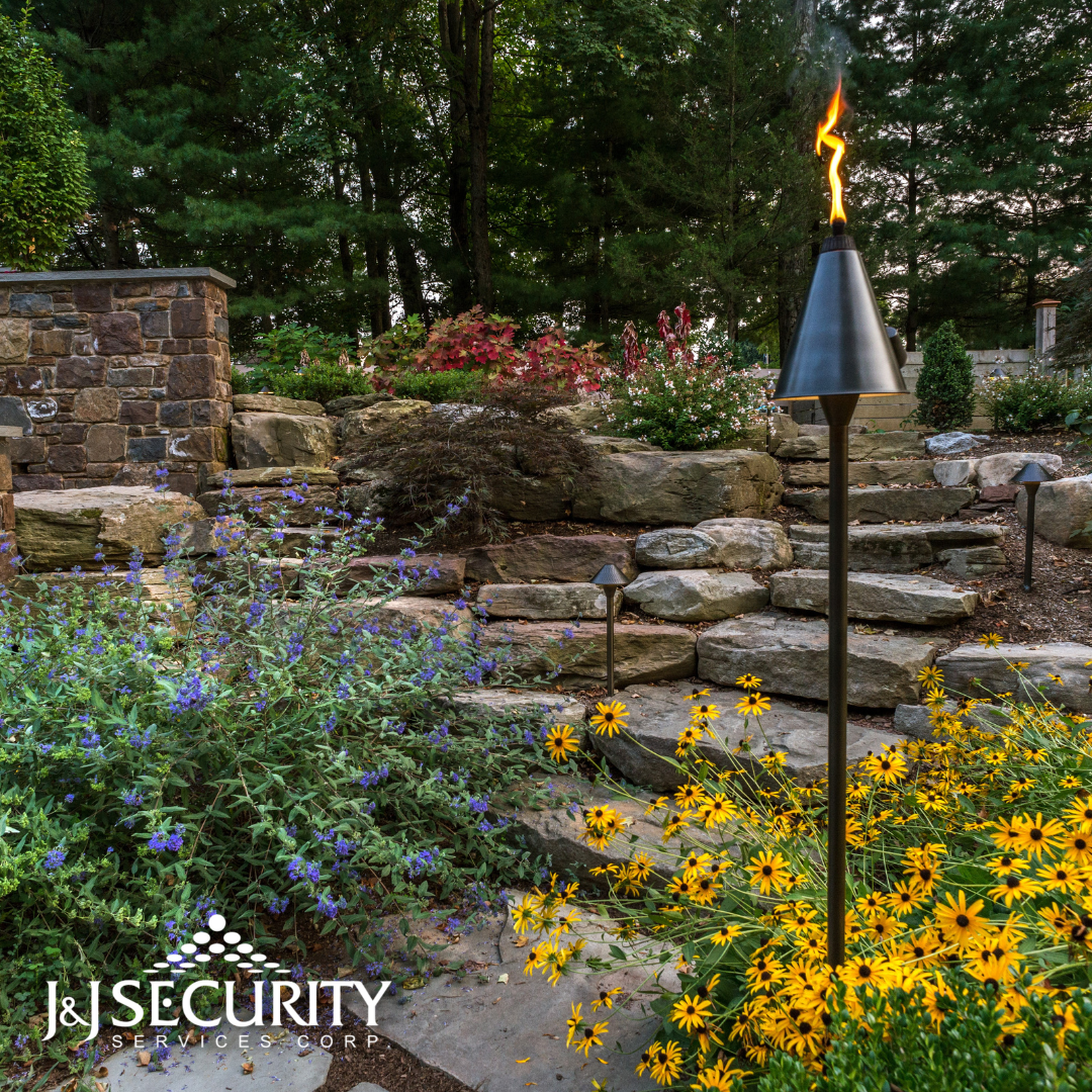 Outdoor garden scene with stone steps, flowers, tiki torch lit, and a stone wall.