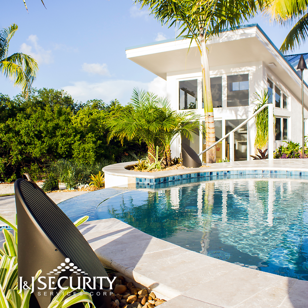 Poolside white modern house with blue water and lush greenery. I&I Security logo in the foreground.