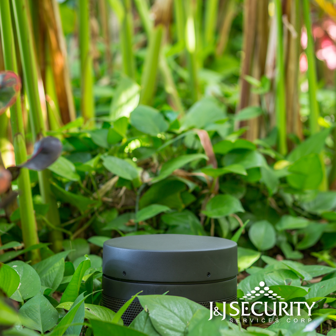 Dark gray outdoor light fixture surrounded by green plants in a garden.