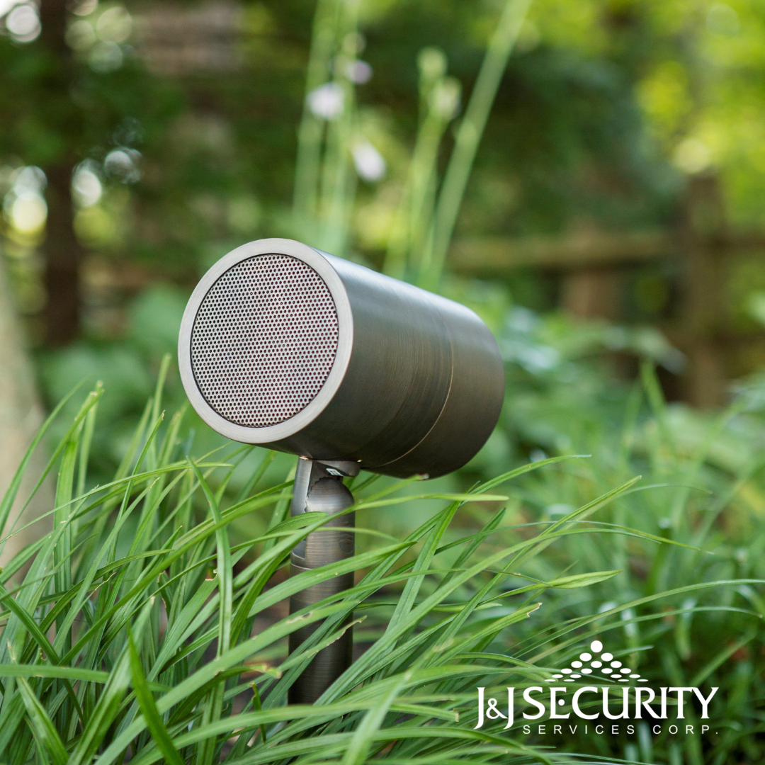 Outdoor speaker with a mesh screen, mounted in garden with green grass.
