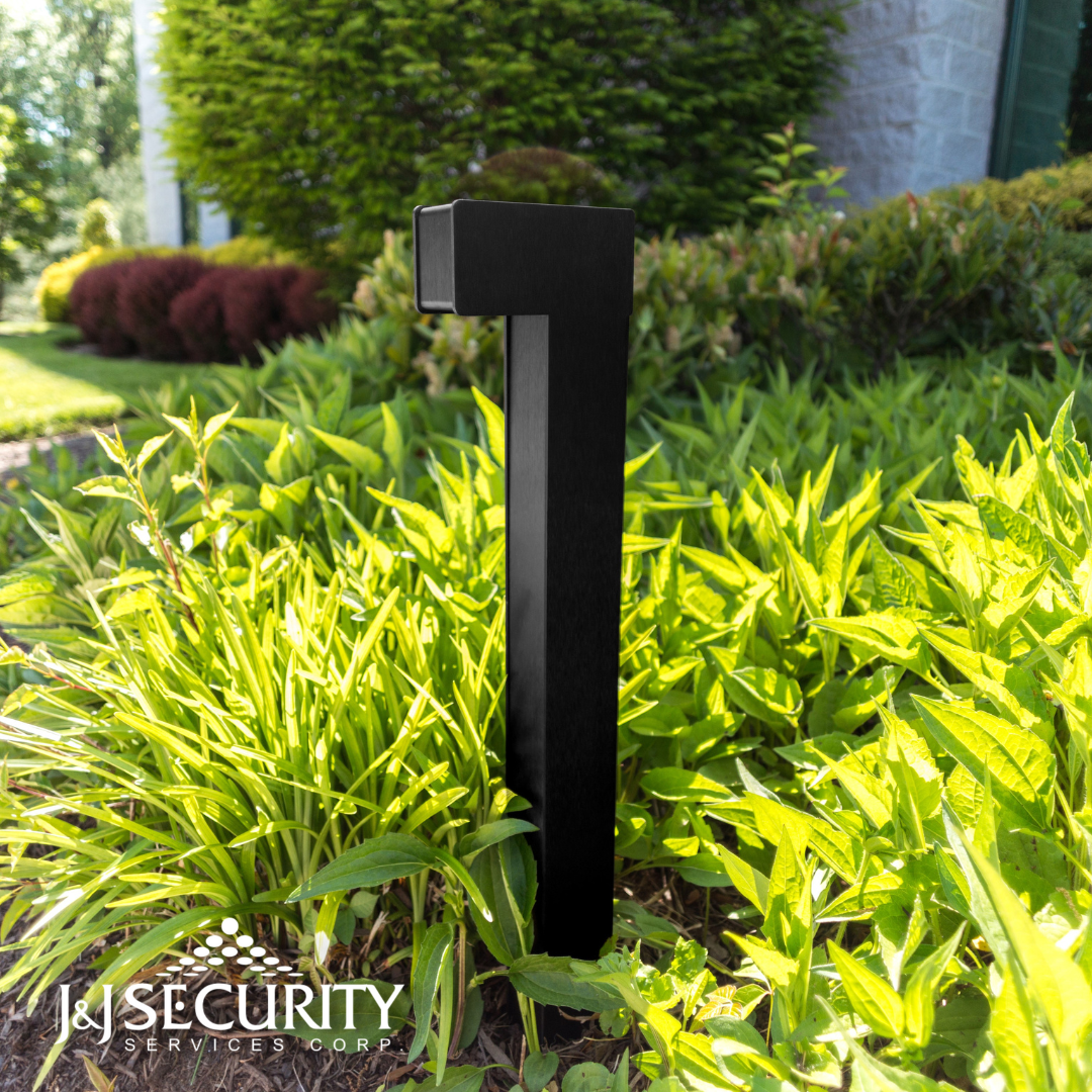 Black security light in a garden, surrounded by green plants.