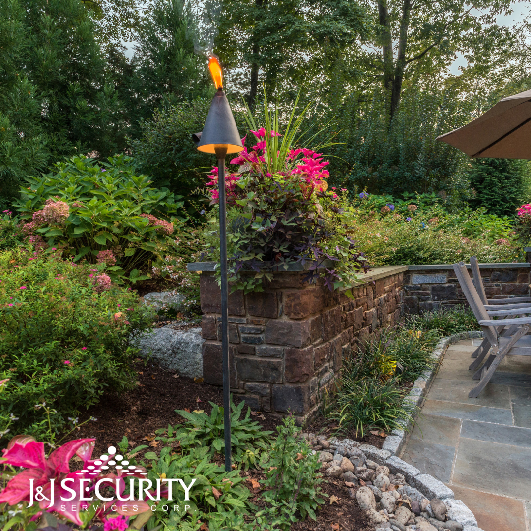 A tiki torch with a flame in a garden, with flowers and patio.