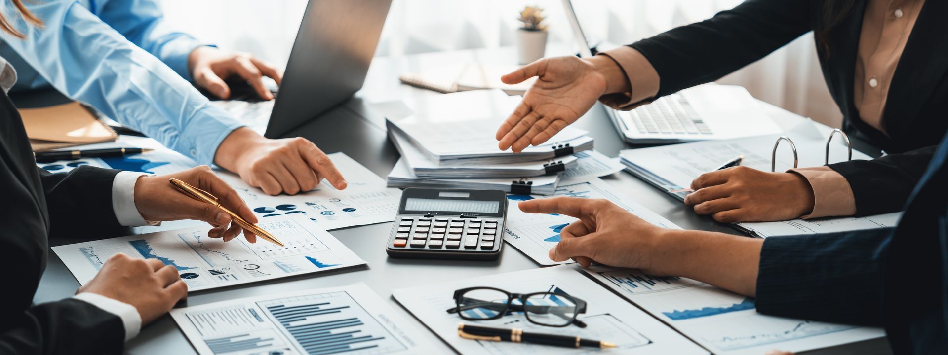 Team reviewing financial reports and charts around a calculator in a meeting.