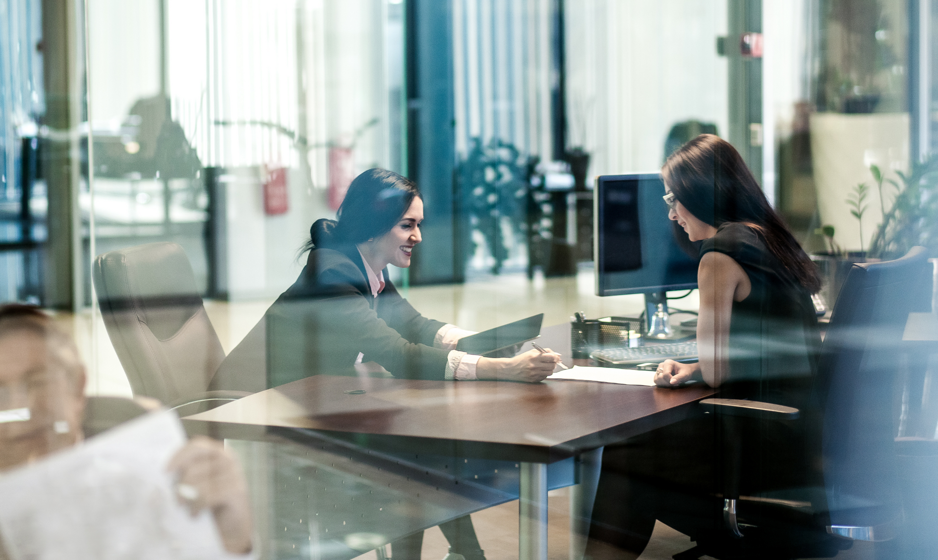 Two women are sitting at a table in an office having a meeting.