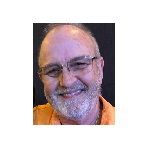 Smiling man with a white beard, wearing glasses and an orange shirt.