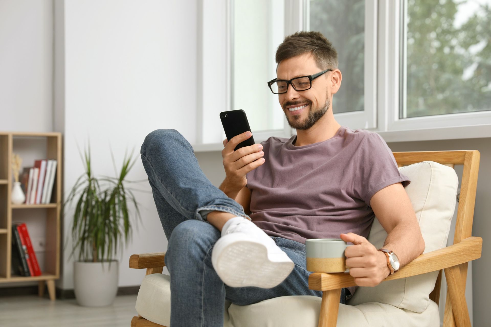 A man is sitting in a chair looking at his cell phone.